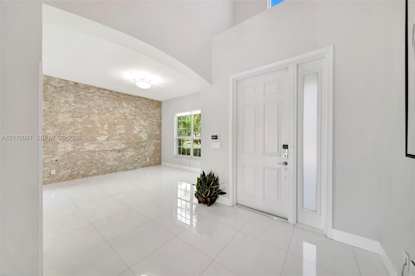 Foyer featuring high ceilings, large-format tile flooring, a prominent textured brick accent wall, and a solid-core entry door with a frosted glass si