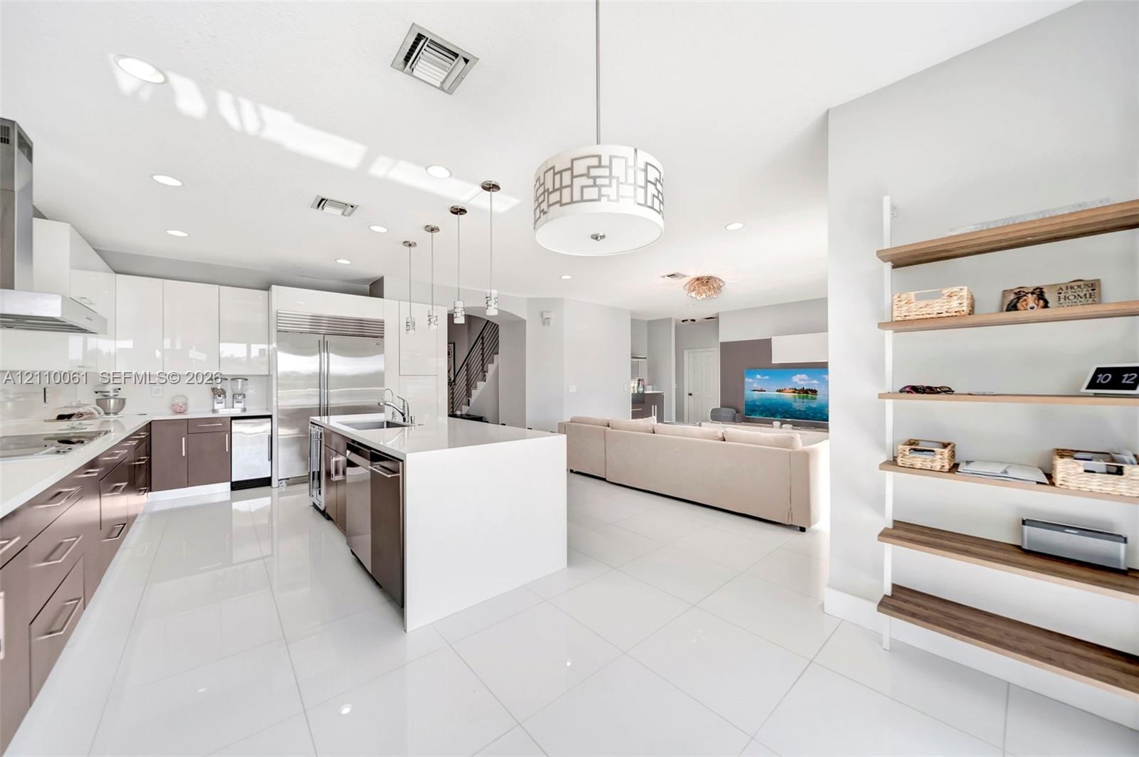 Modern kitchen featuring high-gloss cabinetry, a central island with quartz countertop, stainless steel appliances, polished tile flooring, and integr