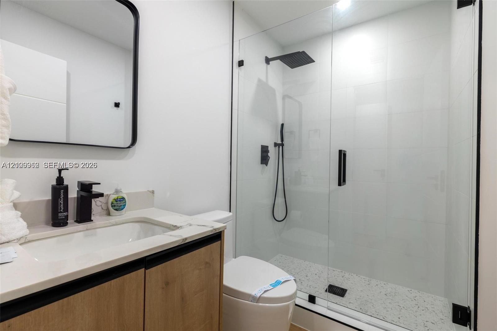 Bathroom featuring a wood-finish vanity with a stone-surface countertop, a frameless glass shower enclosure, matte black fixtures, a rectangular vanit