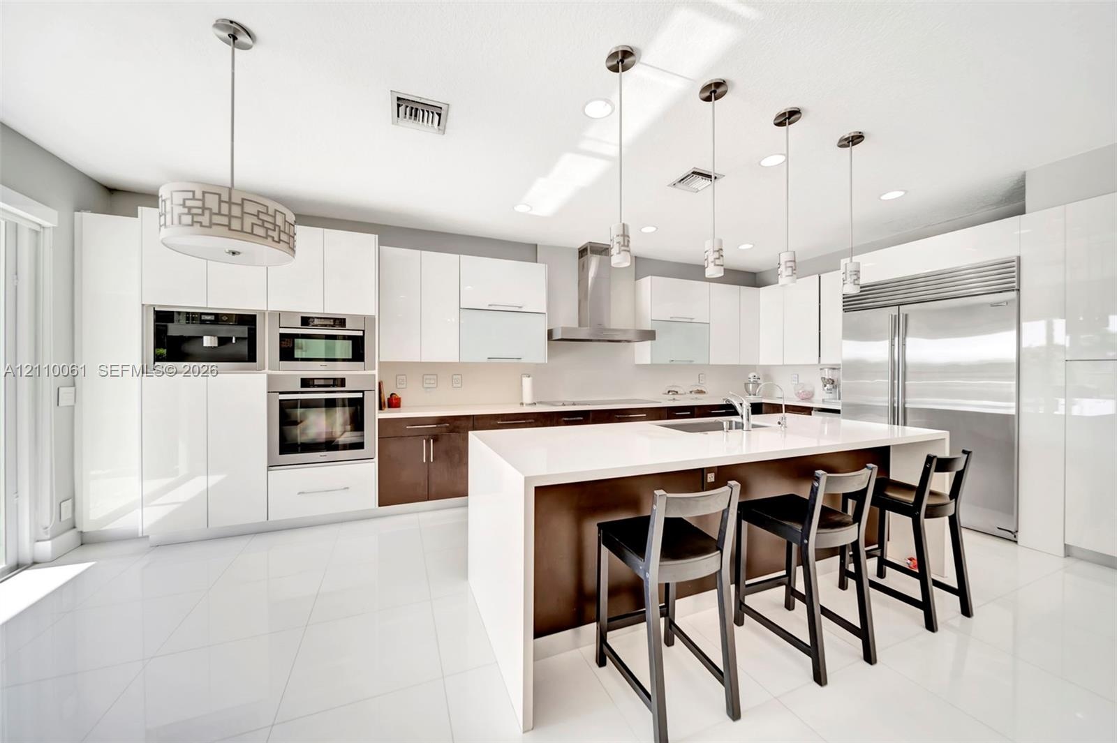 Contemporary kitchen featuring high-gloss cabinetry, a central island with a solid surface countertop, stainless steel appliances, and pendant lightin