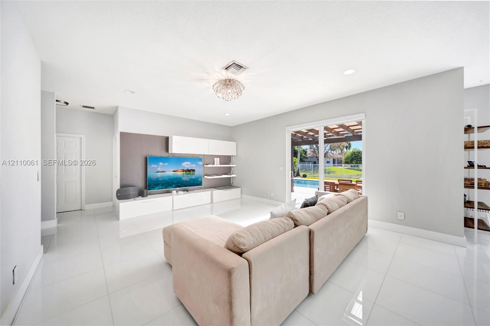Open-concept living space featuring high-gloss tile flooring, recessed lighting, built-in media cabinetry with floating shelving, and sliding glass do