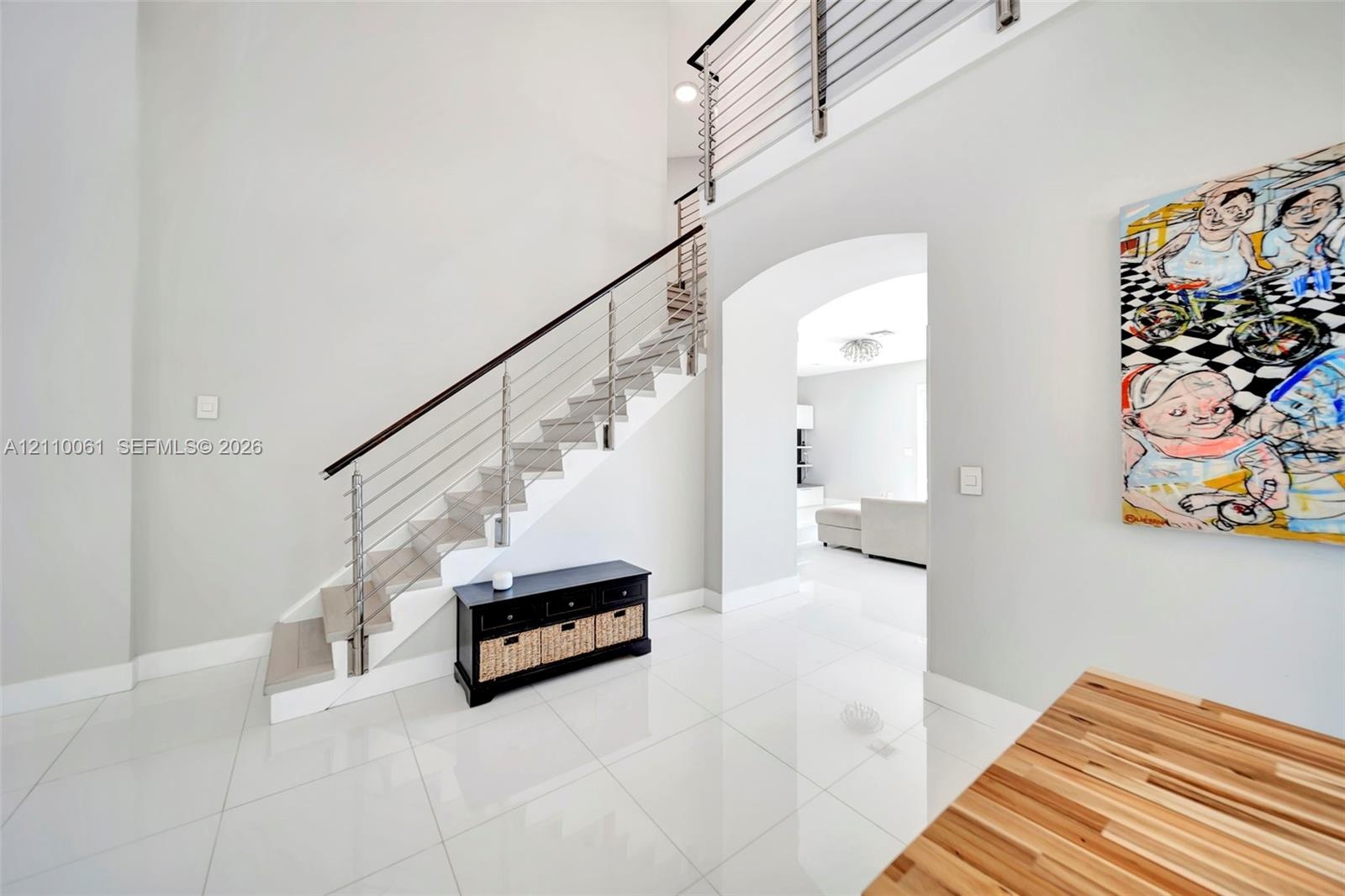 High-ceiling foyer featuring polished large-format tile flooring, a staircase with custom horizontal metal balusters, a dark wood handrail, and a rece