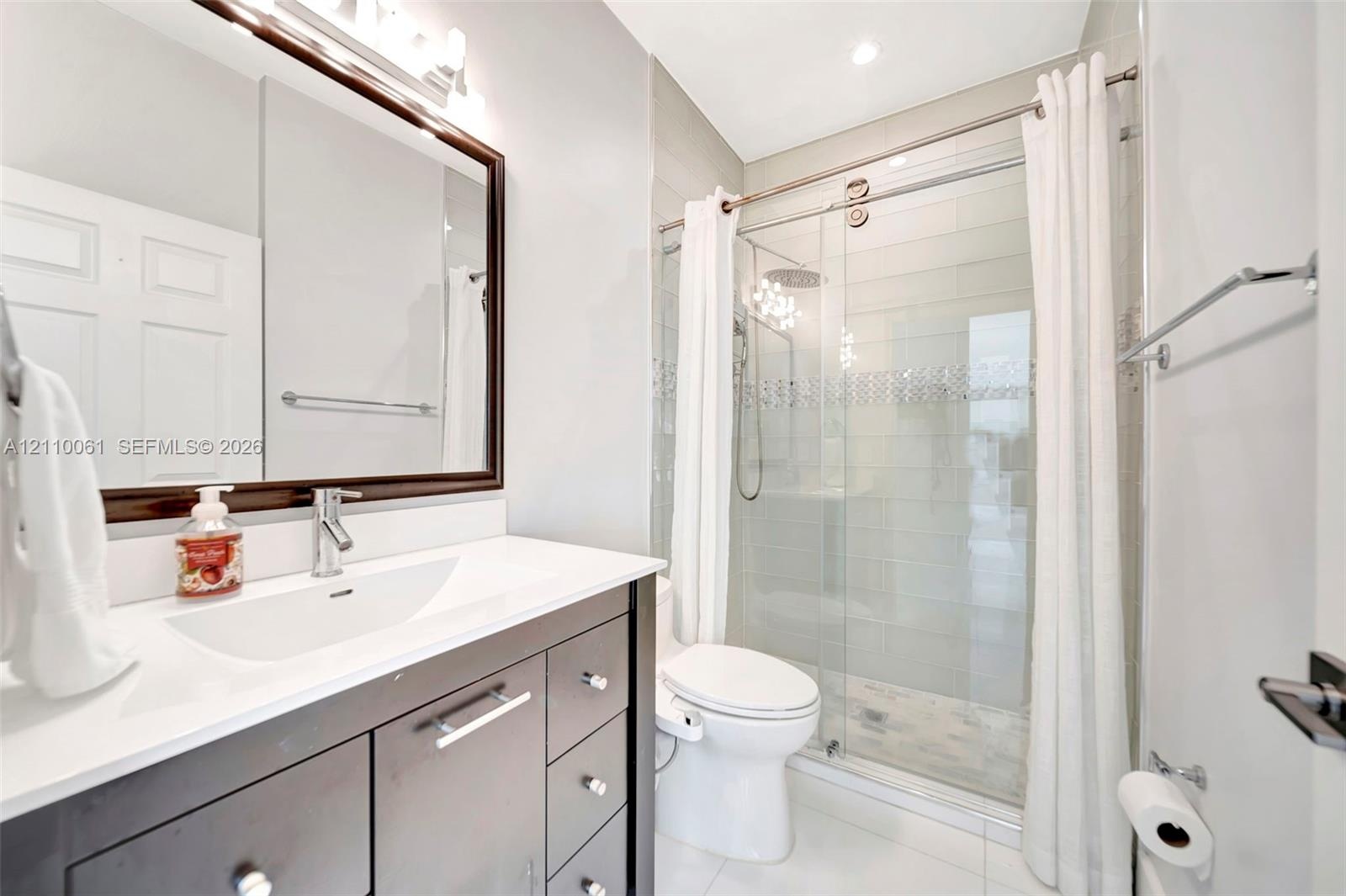 Bathroom featuring a dark-finish vanity with a rectangular sink, quartz countertop, framed wall mirror, and a walk-in shower with sliding glass doors 