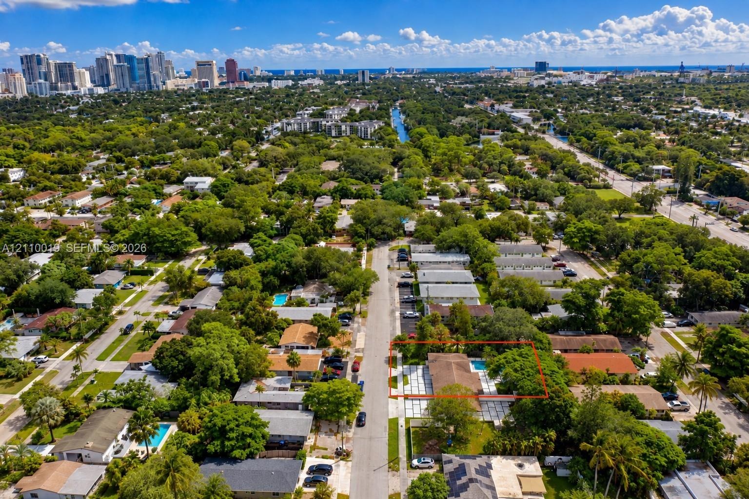 Aerial perspective of property featuring a rectangular pool, concrete paver patio, and mature trees on the lot