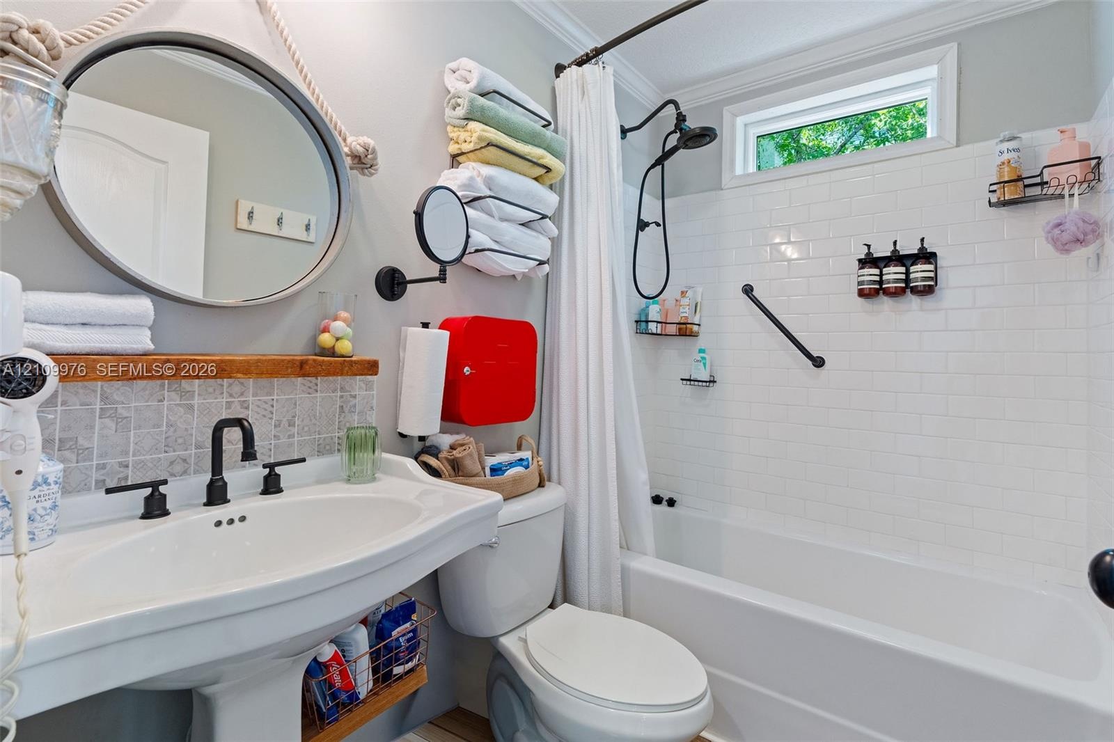 Bright, updated bathroom featuring a curved pedestal sink with matte black fixtures, subway tile shower surround with glass enclosure, circular mirror