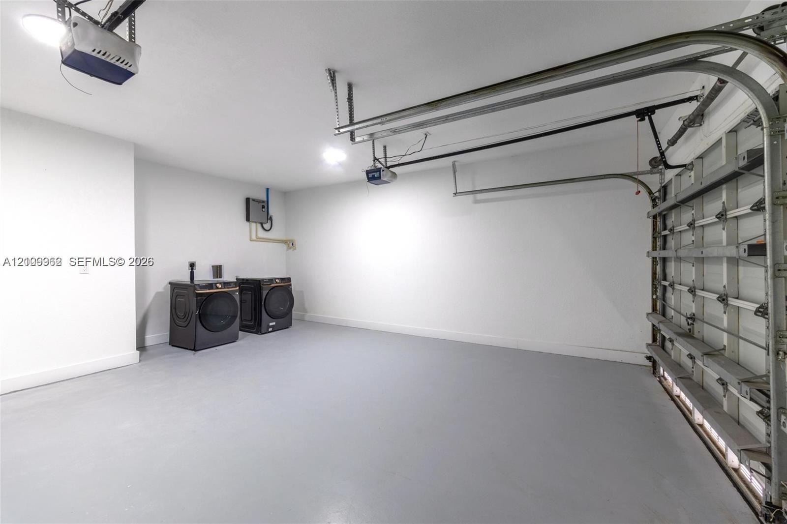 Enclosed garage featuring finished concrete flooring, overhead automatic door opener, and side-by-side laundry appliances