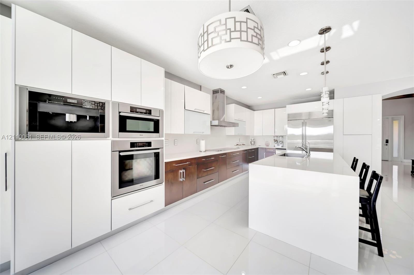 Kitchen featuring two-tone flat-panel cabinetry, a central waterfall-edge island, stainless steel built-in double wall ovens, a coordinating microwave