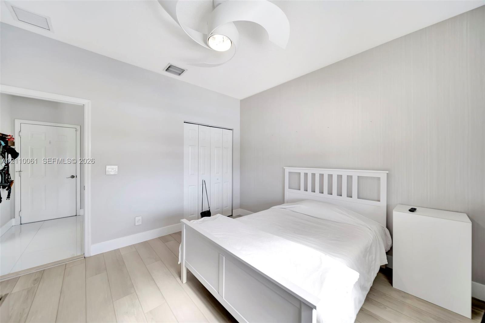 Room featuring wood-finish flooring, textured wall covering, bi-fold closet doors, and a multi-blade ceiling fan with integrated lighting