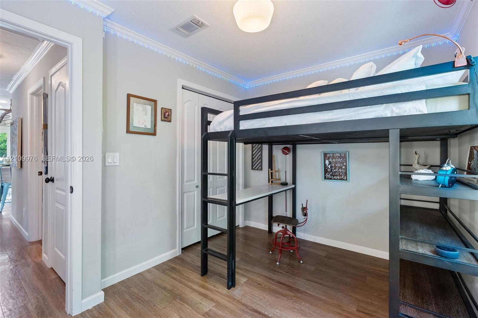 Room featuring wood-finish flooring, crown molding, and a double-door closet