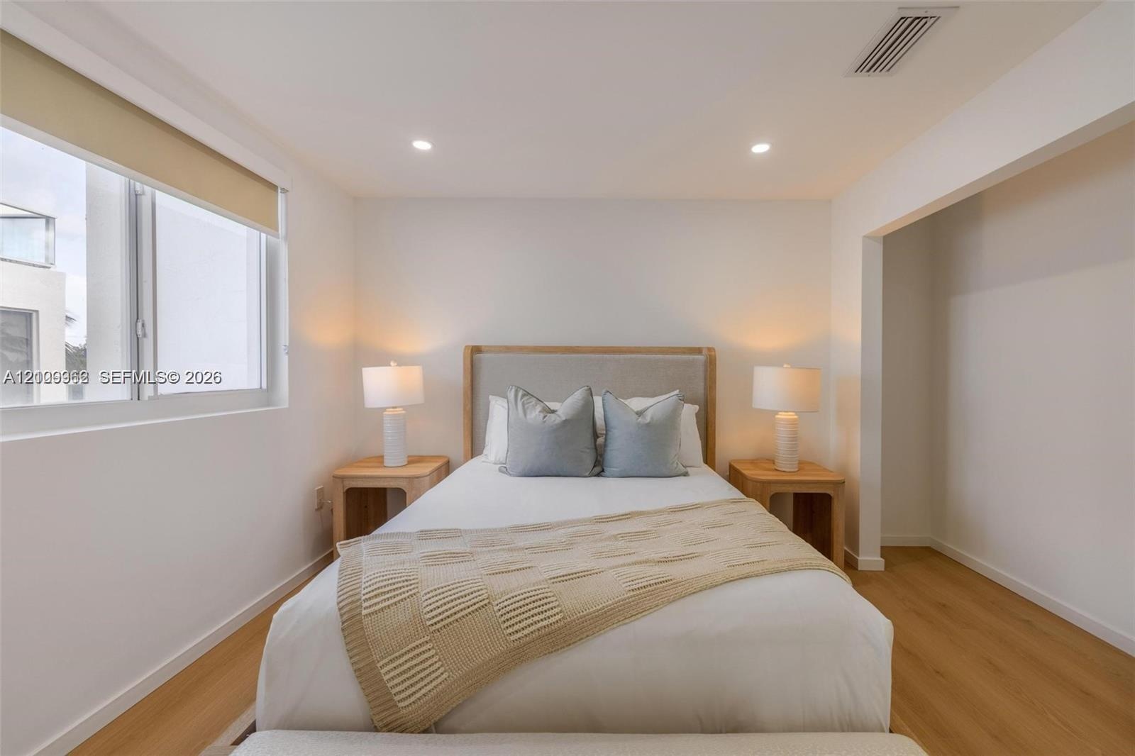 Neutral-toned room featuring wood-finish flooring, recessed lighting, and a large window with roller shade