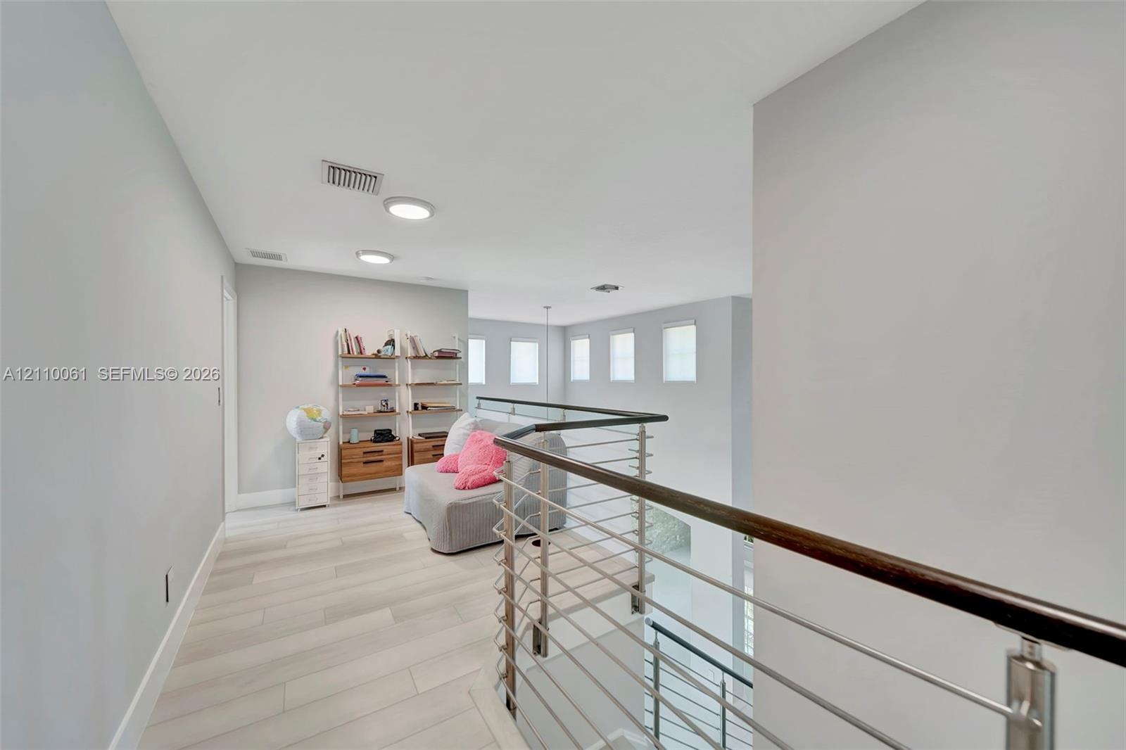 Open floor plan featuring wood-finish flooring, recessed lighting, and a metal horizontal-bar railing with a wood cap