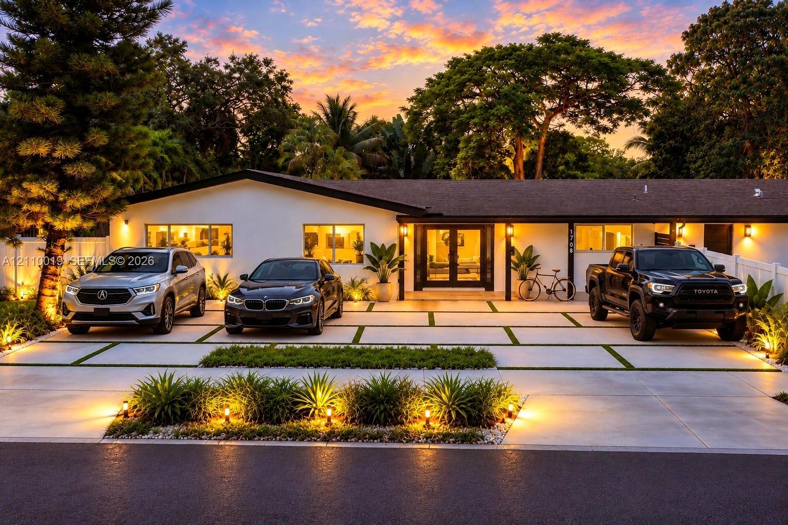 Single-story residence featuring a low-pitched roofline, light-toned exterior finish, segmented concrete driveway with grass inlays, and mature landsc