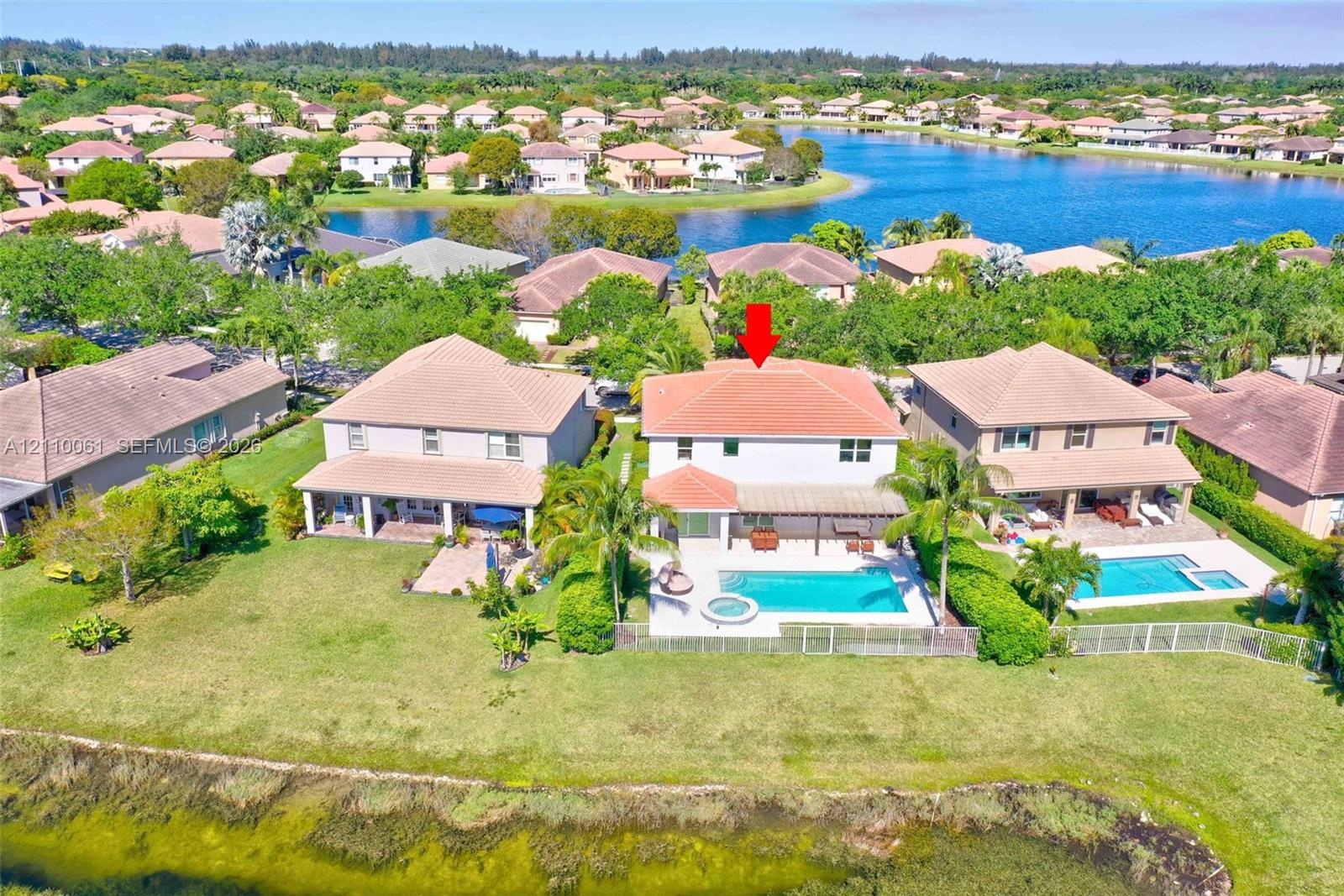 Waterfront residence featuring a two-story architectural design with a terracotta tile roof, expansive manicured lawn, mature landscaping, in-ground s