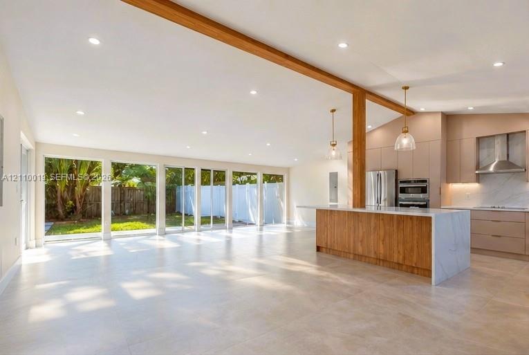 Open-concept space featuring an exposed wood structural beam, floor-to-ceiling sliding glass doors, a large kitchen island with stone-finish waterfall