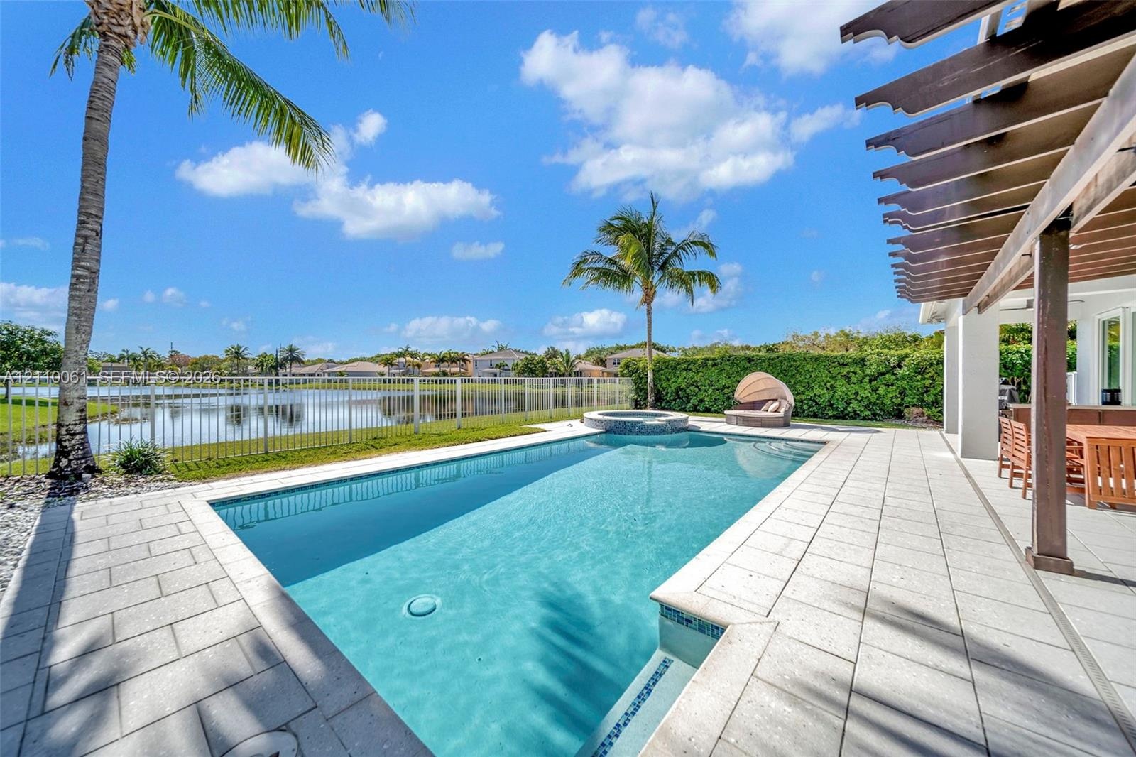 Screened pool area featuring an integrated spa, stone-tile decking, a wooden pergola, and metal perimeter fencing