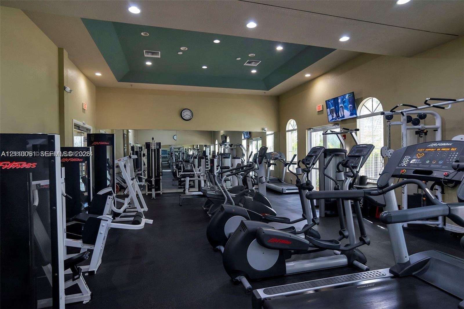 Fitness center featuring a tray ceiling with recessed lighting, wall-to-wall mirrors, and arched windows