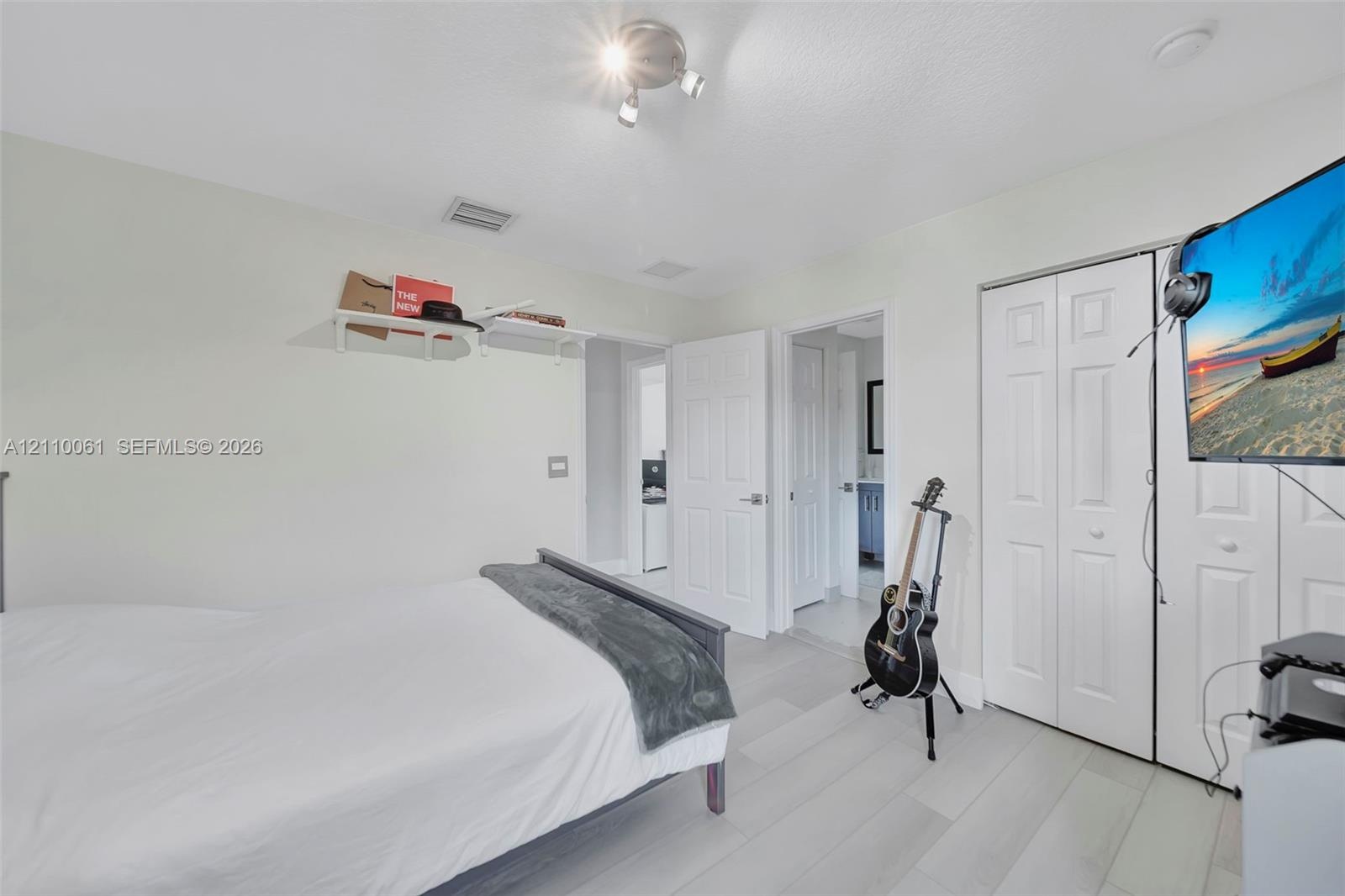 Neutral-toned wood-finish flooring, white paneled closet doors, adjustable multi-head track lighting, and built-in wall shelving