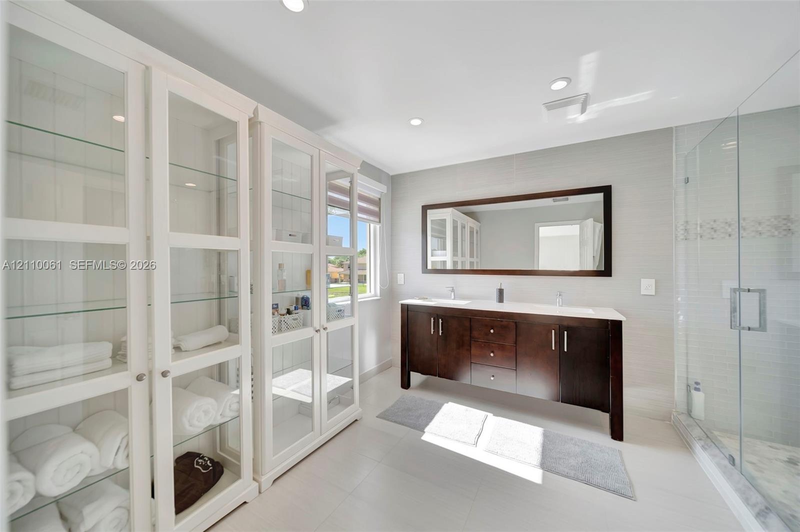 Double vanity with a dark wood-finish cabinet and surface countertop, glass-enclosed shower with tile surround, and extensive built-in cabinetry featu