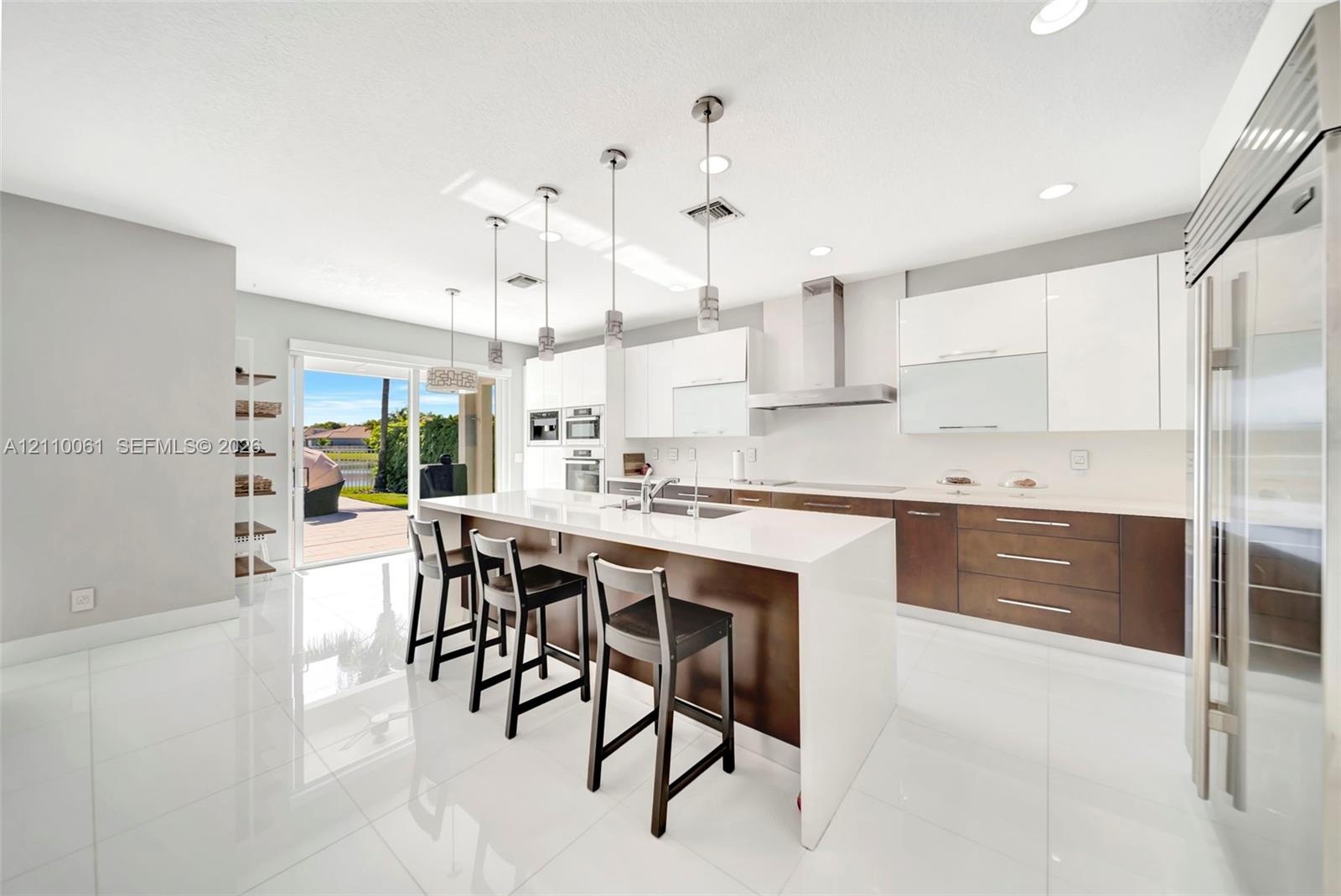 Contemporary kitchen featuring an expansive waterfall-edge island, two-tone cabinetry with gloss-finish uppers, stainless steel professional-grade app