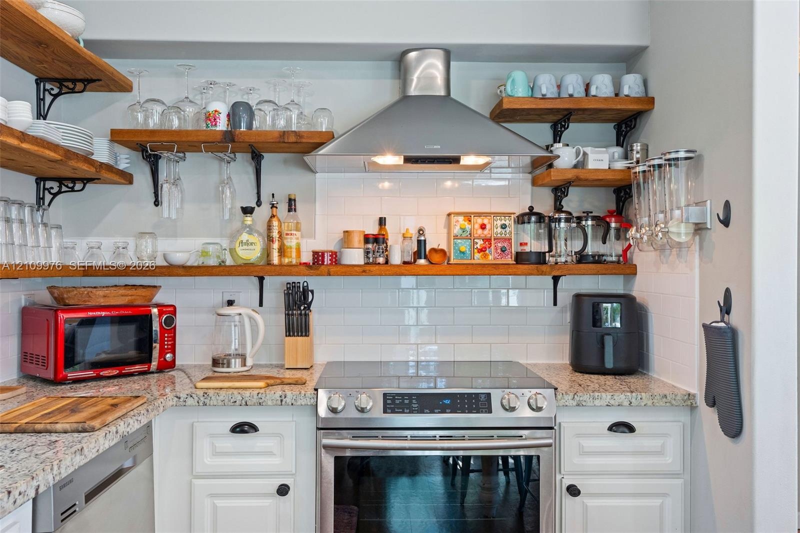 Kitchen area featuring white shaker-style cabinetry, natural stone countertops, white subway tile backsplash, stainless steel range with overhead vent