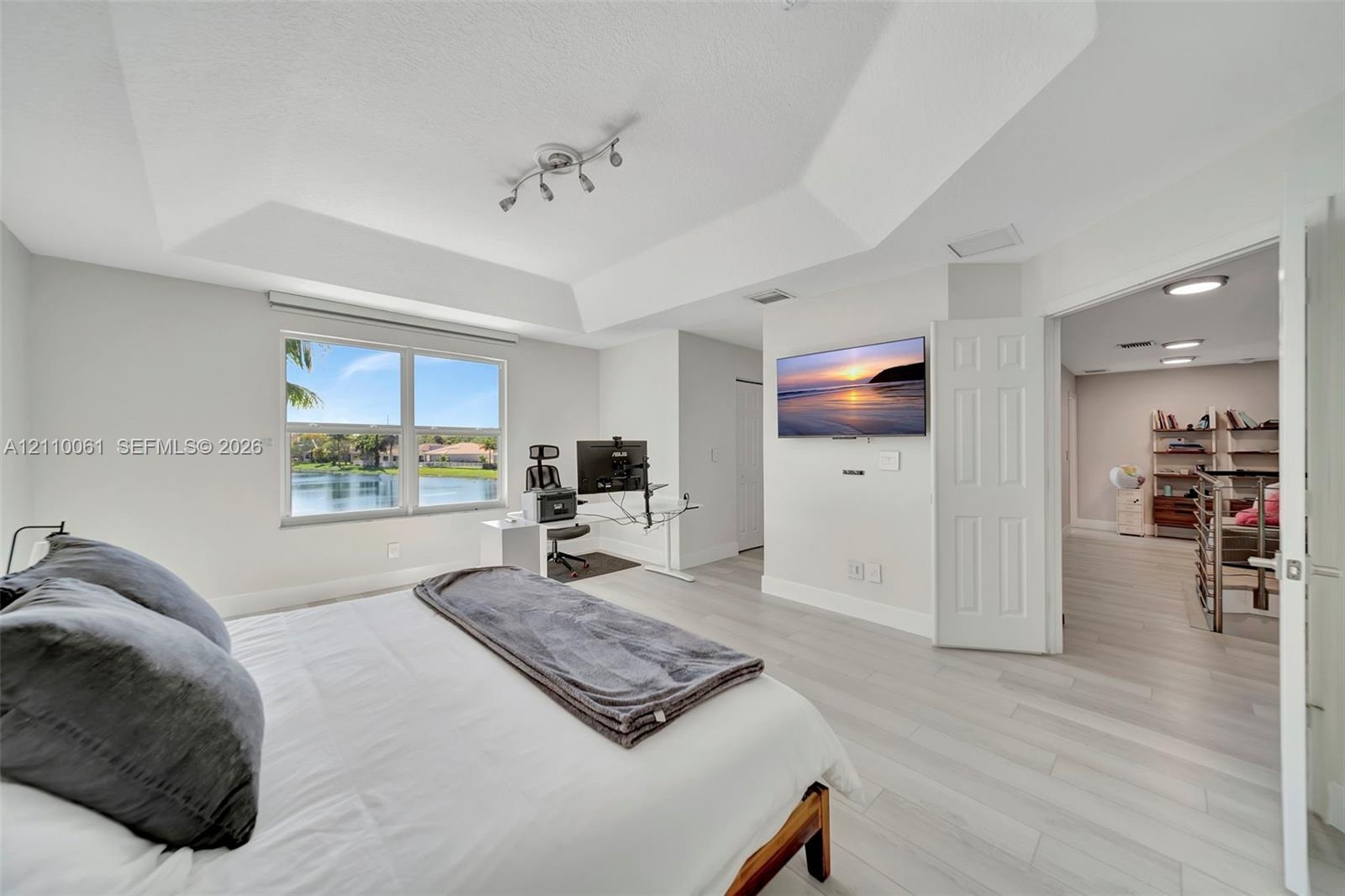 Tray ceiling with multi-directional track lighting, light-toned wood-finish flooring, and large window with water exposure