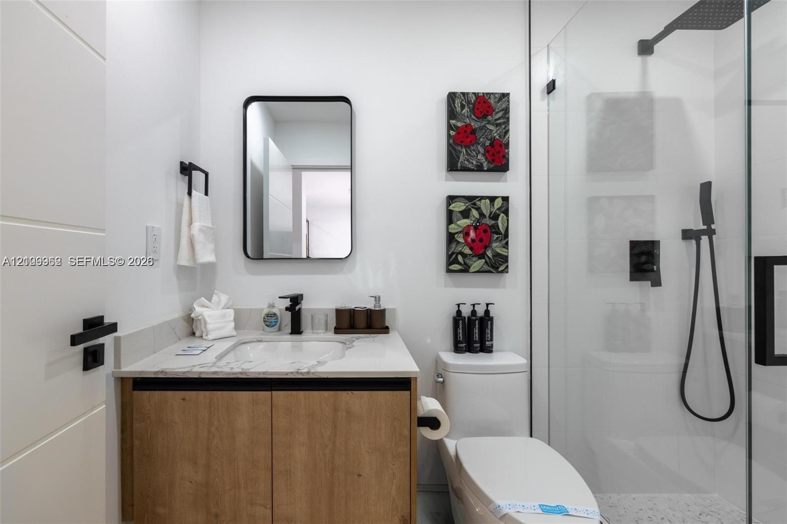 Modern vanity with a composite countertop and integrated basin, rectangular wall-mounted mirror, matte black plumbing fixtures, glass-enclosed shower,