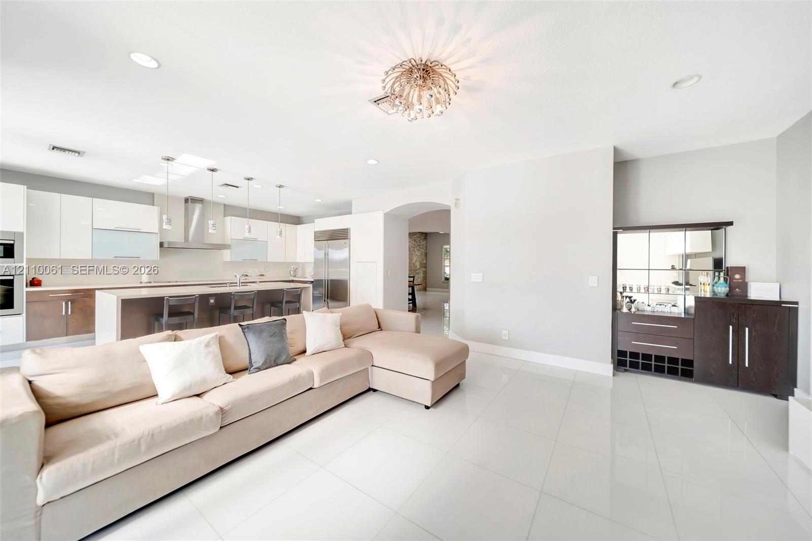 Open-concept space featuring polished tile flooring, two-tone cabinetry with an integrated breakfast bar, built-in stainless steel appliances, recesse