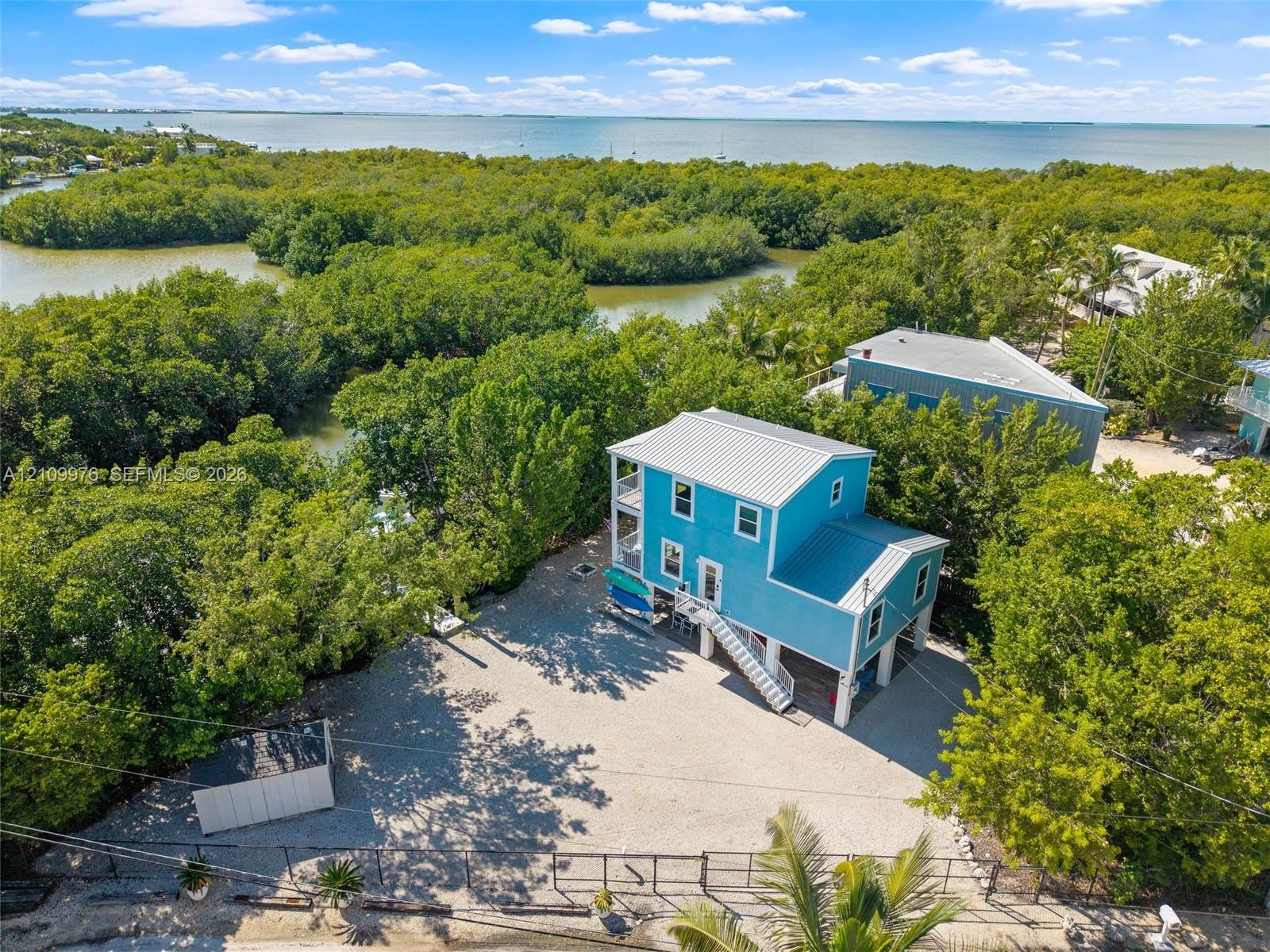 Elevated residence featuring a metal roof, exterior stairway, stone-surface driveway, and onsite storage structure, situated within proximity to coast