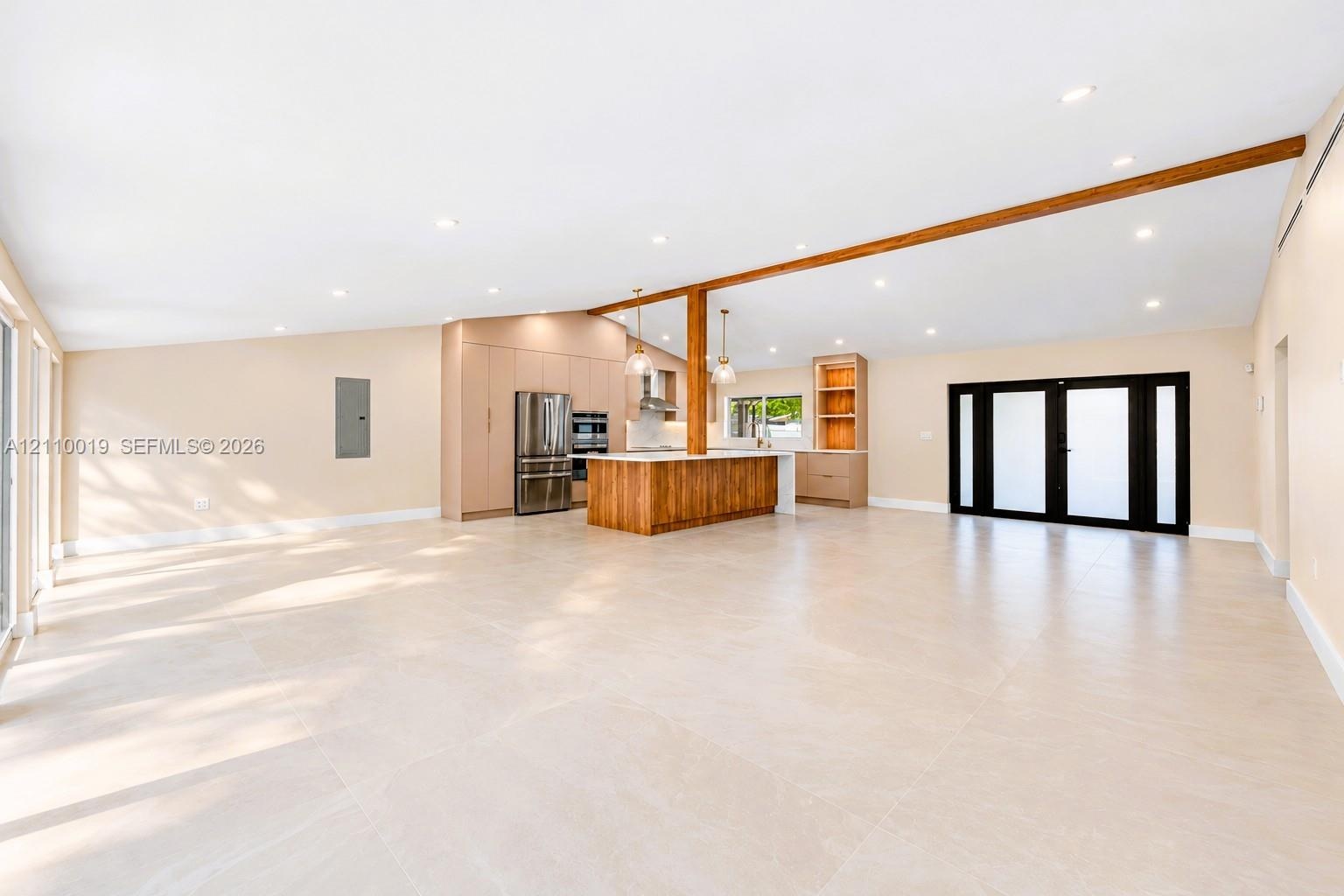 Expansive open-concept interior featuring vaulted ceilings, large-format tile flooring, a wood-accented center island, built-in cabinetry, and black-f