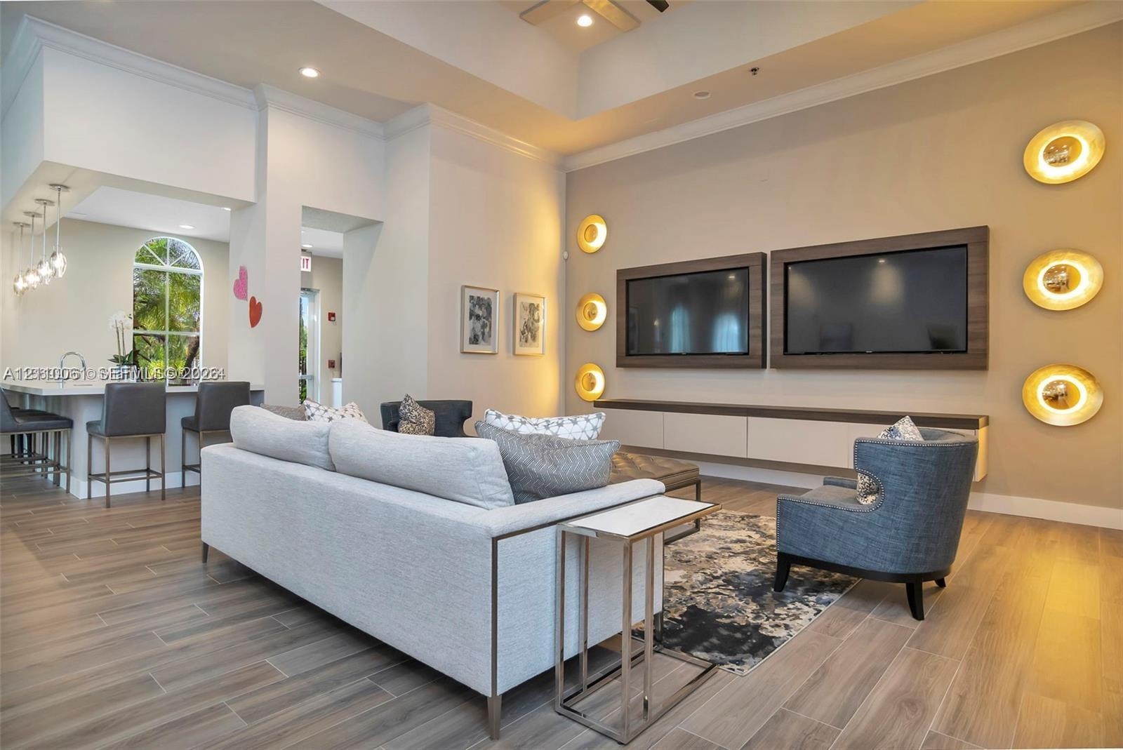 Open-concept living space featuring high tray ceilings, wood-finish flooring, a wall-mounted media console with built-in cabinetry, custom circular wa