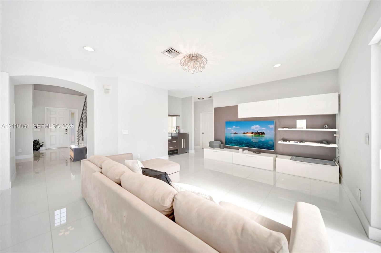 Large-format polished tile flooring, integrated wall-mounted media cabinetry with open shelving, recessed lighting, arched entryway, and decorative fl