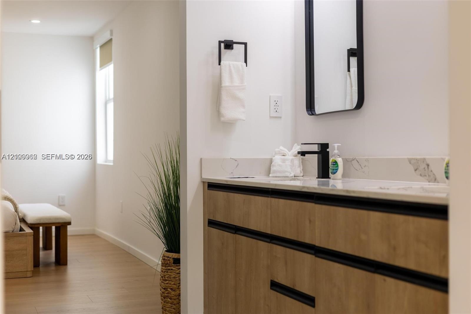 Floating vanity with wood-finish cabinetry, stone countertop, matte black faucet, and rectangular mirror with black frame