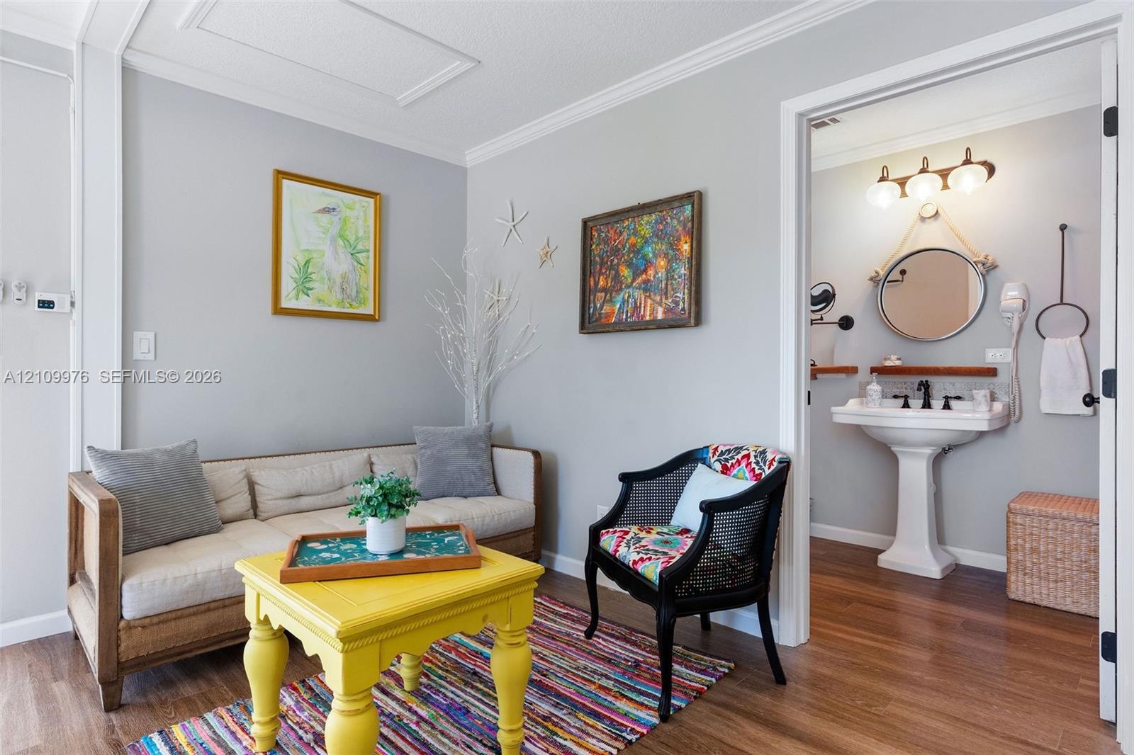 Interior space featuring wood-finish flooring and crown molding, with an opening to a bathroom equipped with a pedestal sink, three-bulb vanity lighti