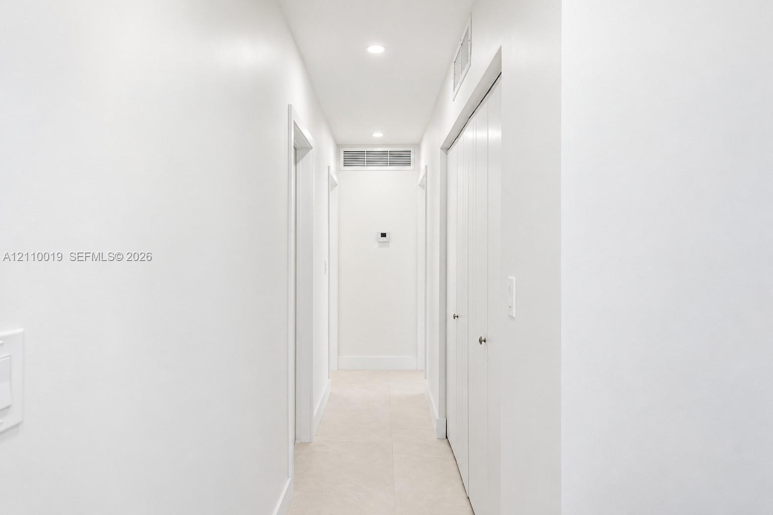 Hallway featuring neutral tile flooring, recessed lighting, and white bi-fold closet doors
