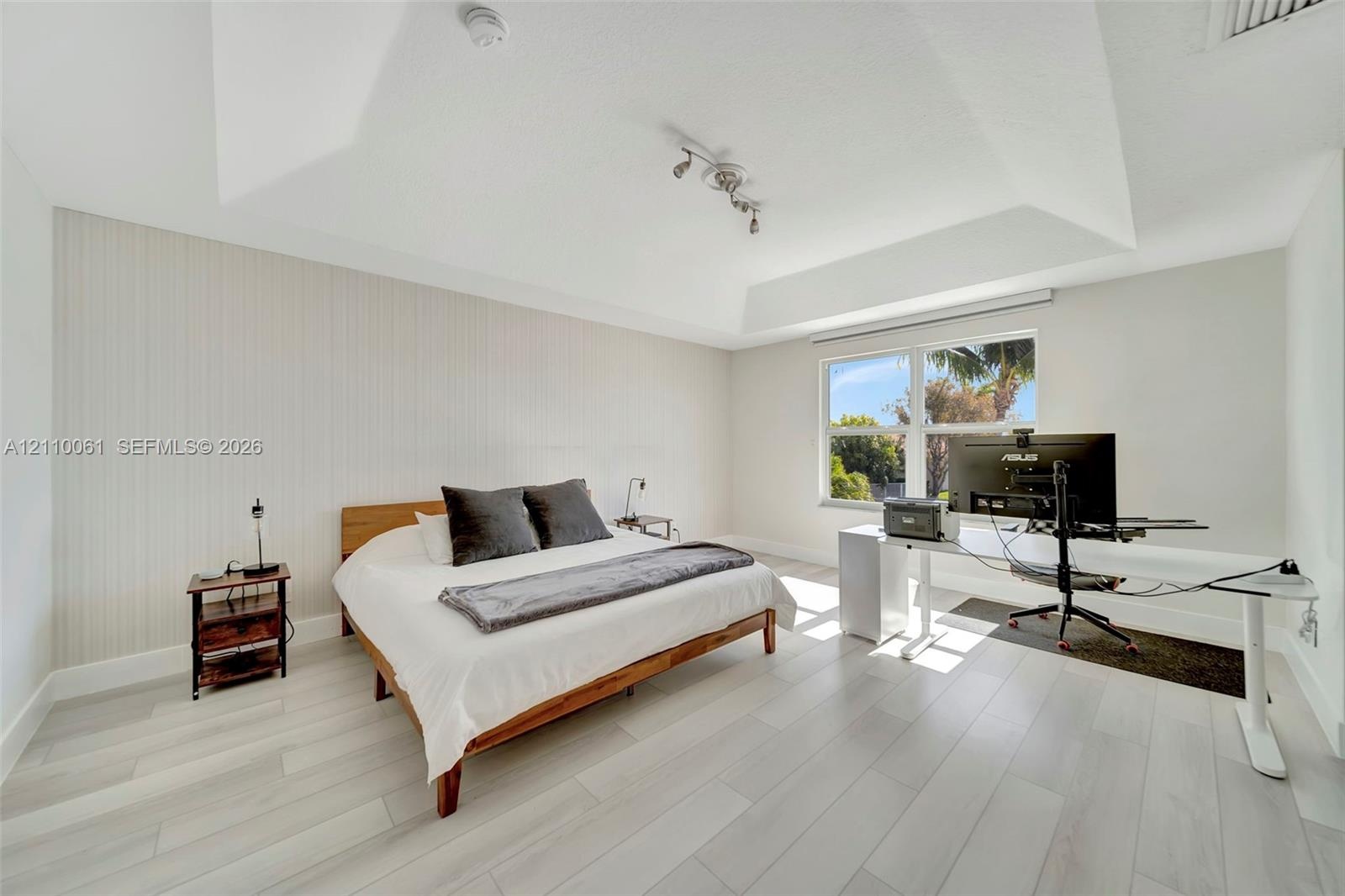 Tray ceiling, vertical panel accent wall, light-toned wood-finish flooring, and multi-pane window