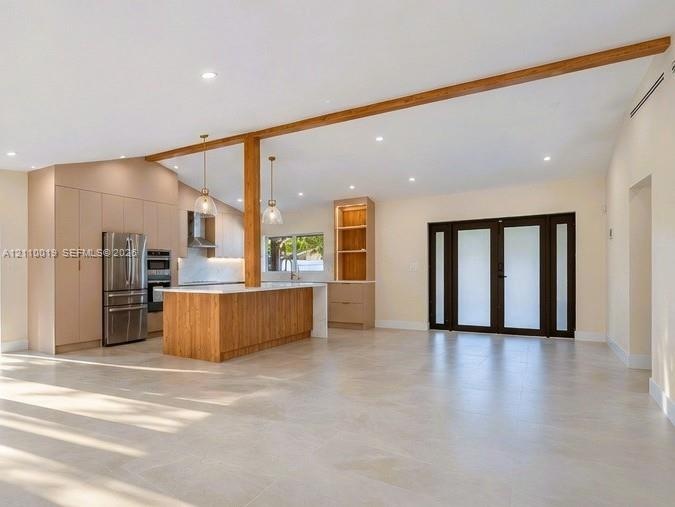 Open-concept interior featuring vaulted ceilings with exposed wood beams, large-format tile flooring, a kitchen island with wood-finish cabinetry, bui