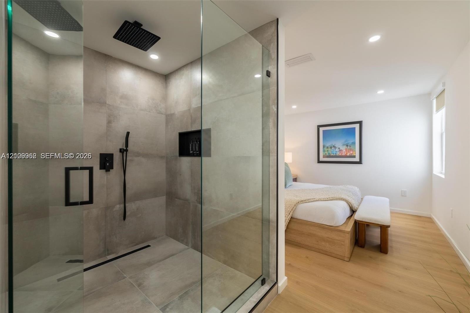 Walk-in shower featuring large-format stone-finish tile, glass enclosure, recessed wall niche, and matte black rainfall showerhead with handheld attac