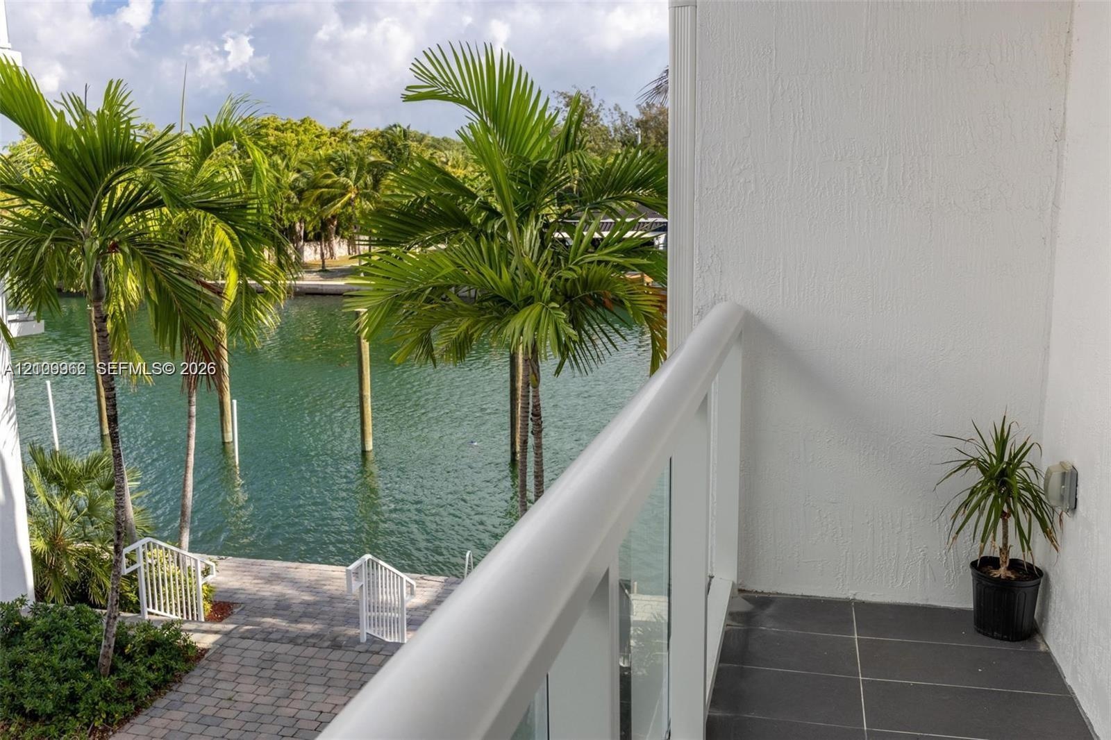 Covered balcony featuring glass railing, tiled flooring, and waterfront access with a paved walkway