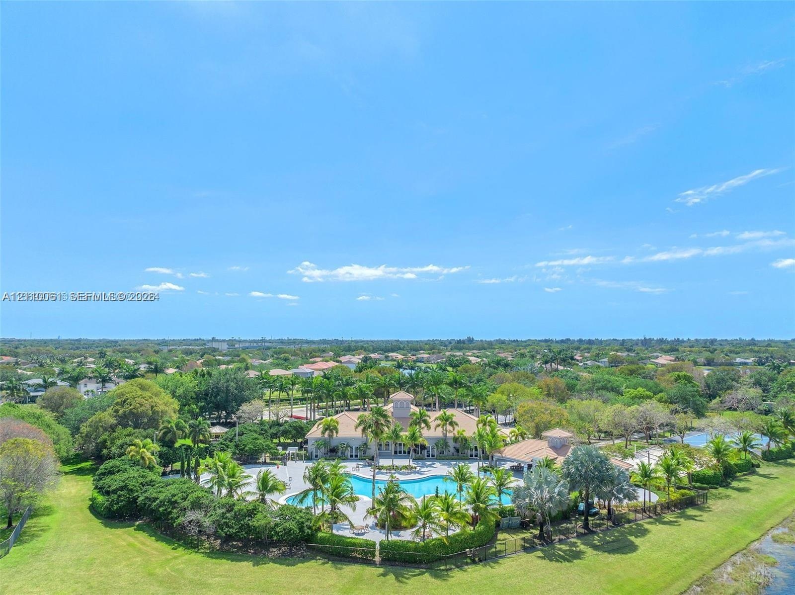 Aerial view of a sprawling estate featuring a large swimming pool, expansive manicured lawn, established palm trees, and professional landscaping