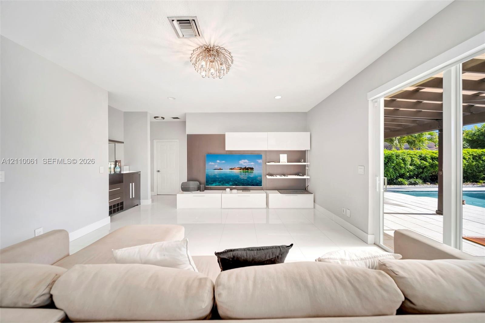 Large-format tile flooring, built-in media cabinetry with shelving, recessed lighting, and sliding glass doors leading to a covered patio with an outd