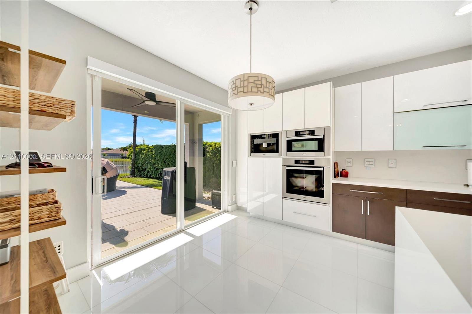 Kitchen featuring high-gloss white cabinetry, dual-tone lower storage, built-in stainless steel double wall ovens, large-format tile flooring, and sli