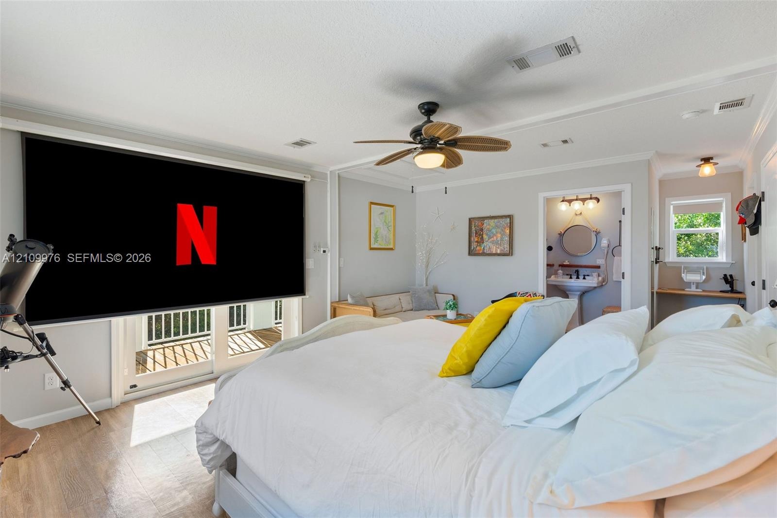 Room featuring wood-finish flooring, a ceiling fan with integrated lighting, glass sliding doors leading to a balcony, and an attached bathroom with a