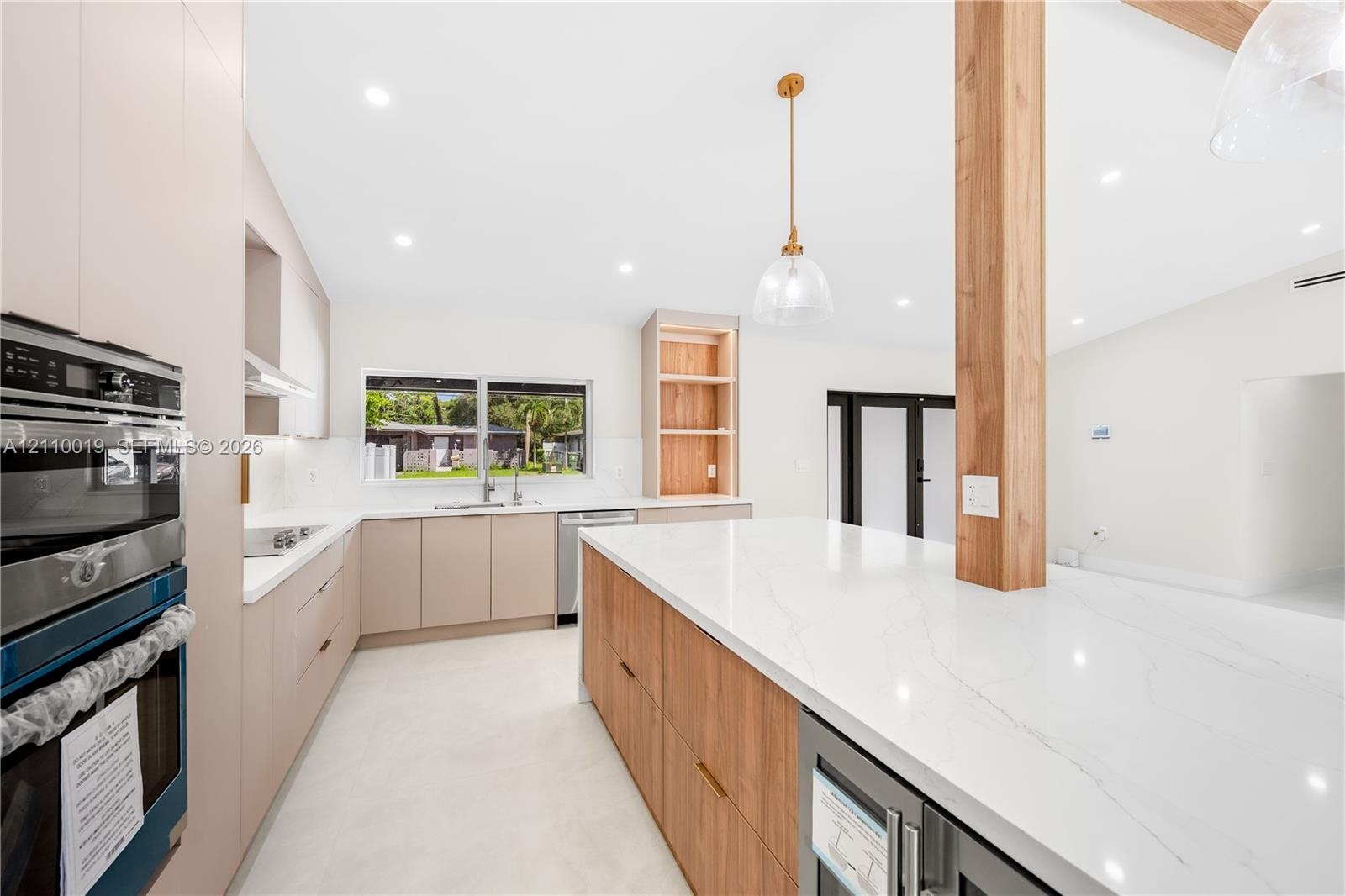 Kitchen featuring flat-panel cabinetry, a spacious stone-surfaced island, integrated stainless steel appliances, a structural wood pillar, and recesse