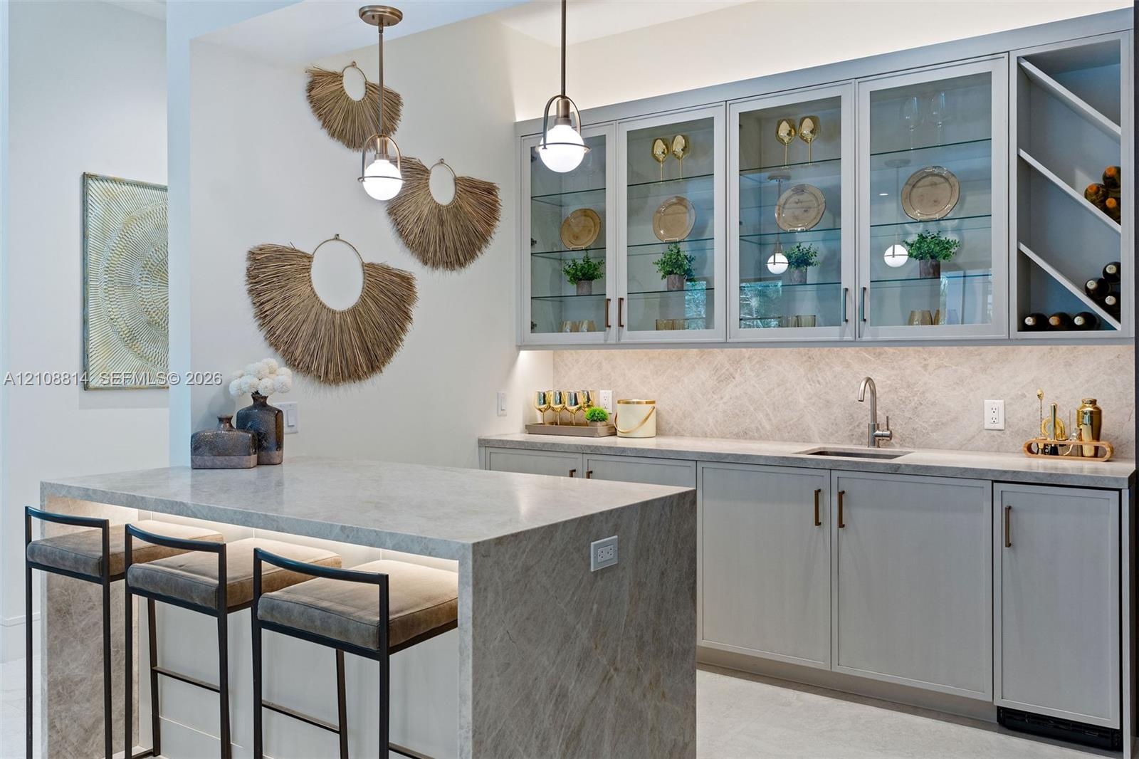 Custom cabinetry with glass-front display doors and wine storage, stone-topped island with waterfall edge, herringbone-patterned tile backsplash, unde