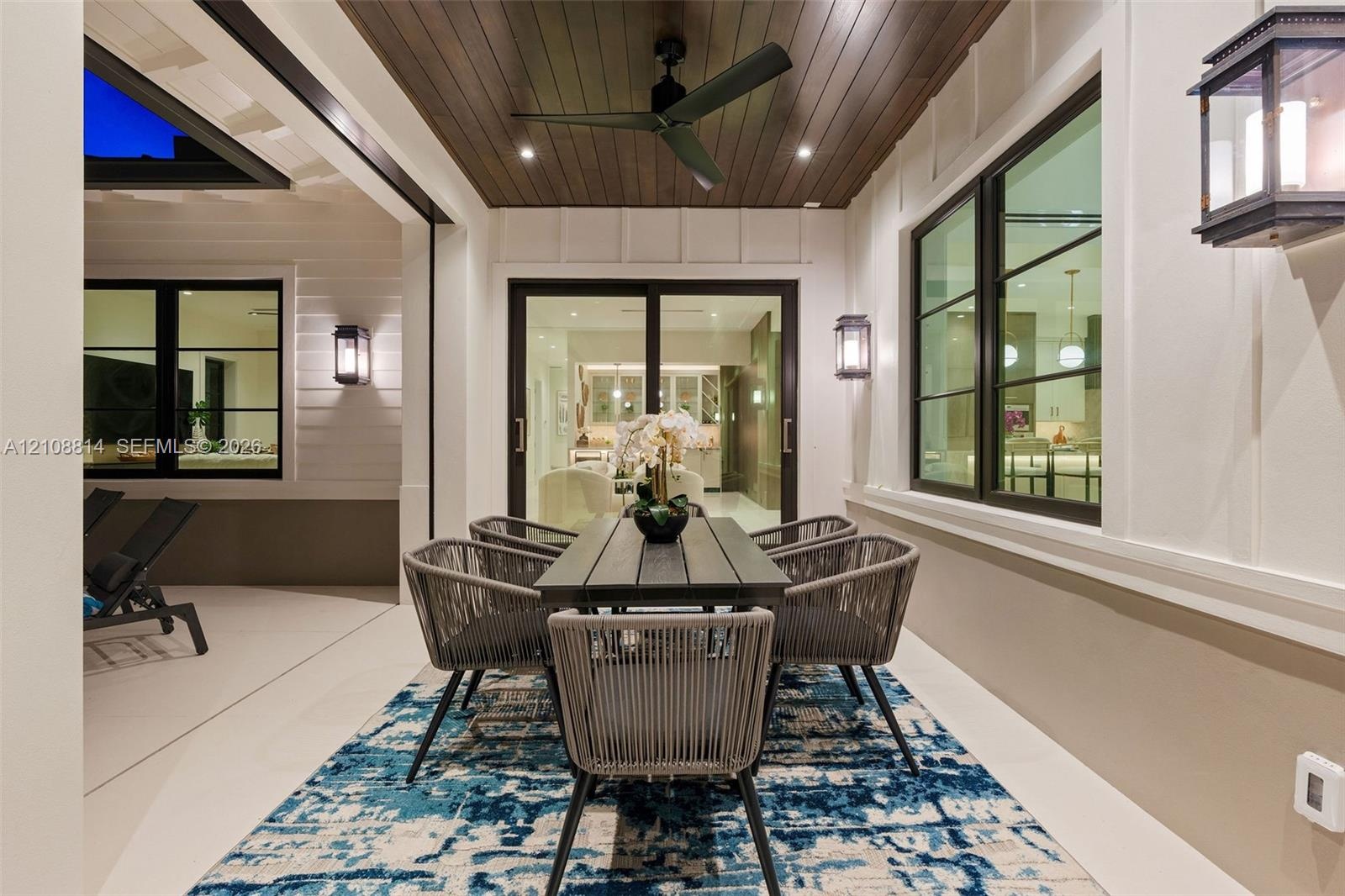 Covered patio featuring a wood-plank ceiling, matte black ceiling fan, recessed lighting, wall-mounted exterior lanterns, and multi-panel sliding glas