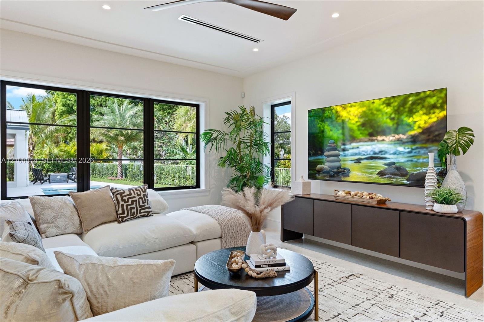 Living space featuring black-framed picture windows, recessed lighting, ceiling fan with wood-finish blades, and custom built-in cabinetry with a curv