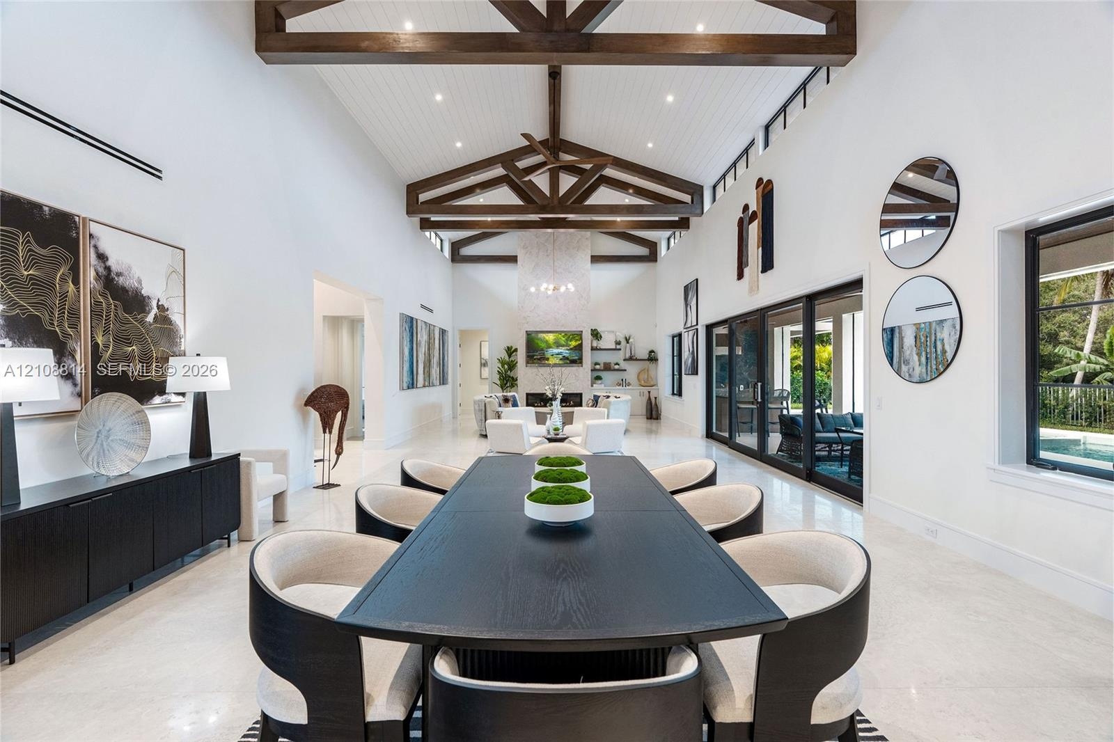 Vaulted ceilings with exposed wood beams, polished stone flooring, custom built-in cabinetry, floor-to-ceiling sliding glass doors, and a decorative t
