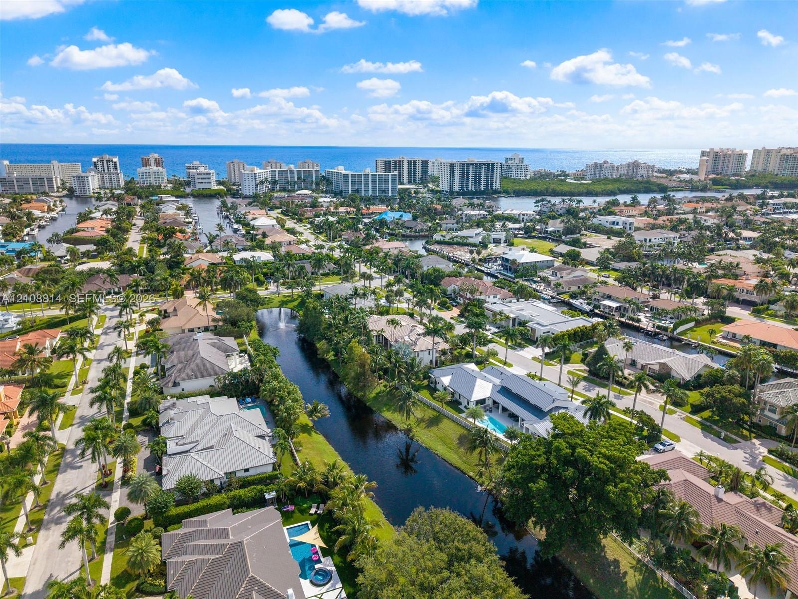Aerial perspective of a coastal residential community featuring a network of canals, private swimming pools, mature palm trees, and residential archit