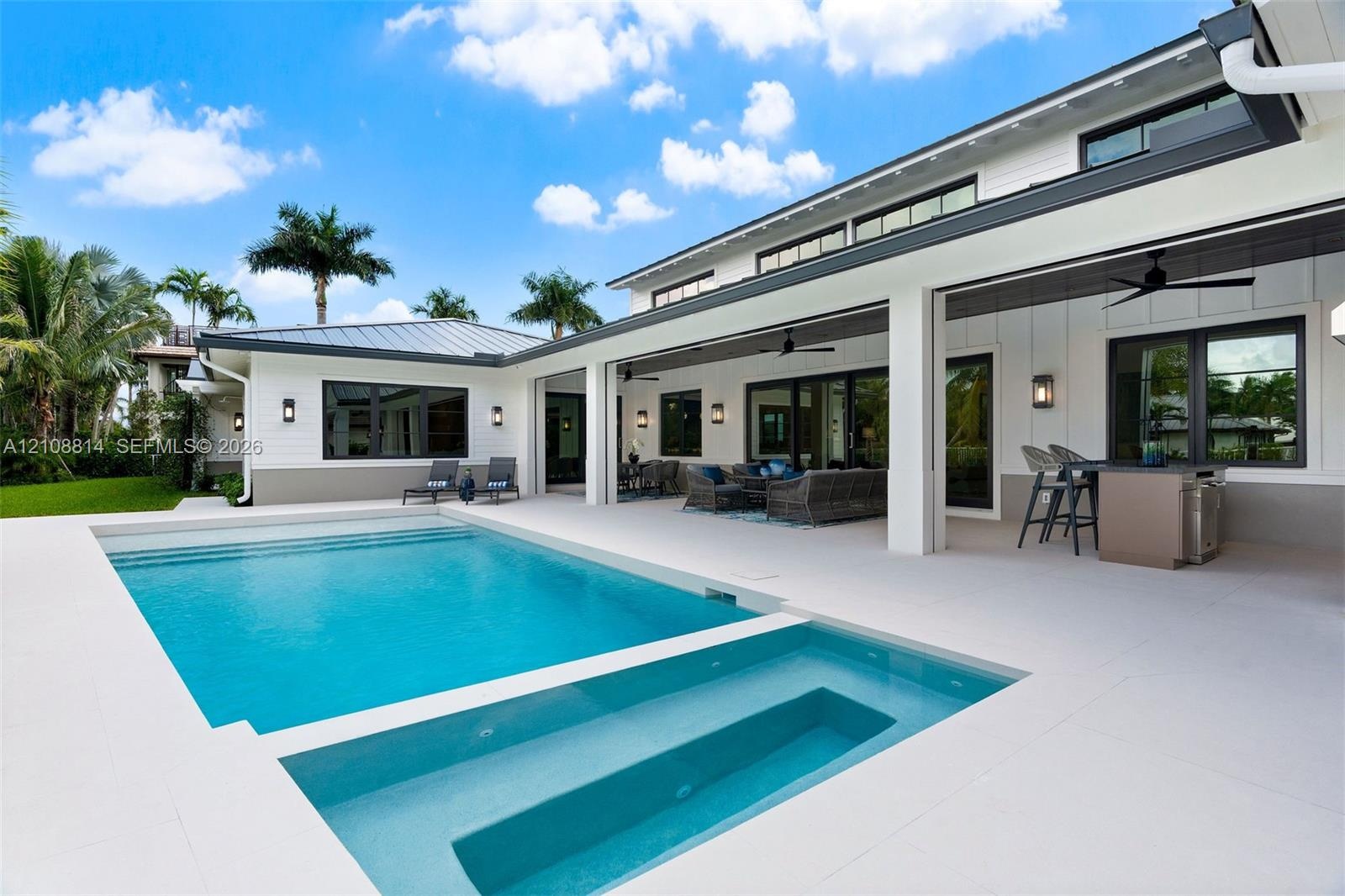 Modern exterior featuring board-and-batten siding, a covered patio with integrated ceiling fans, a built-in outdoor kitchen, and a swimming pool with 