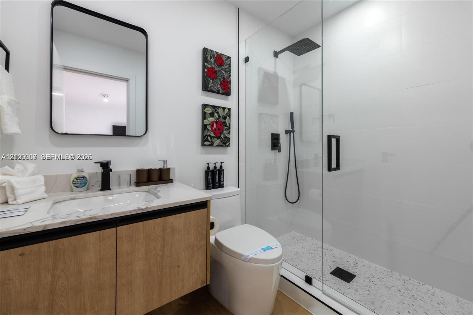 Floating wood-finish vanity with a composite countertop and integrated basin, matte black wall-mounted faucet, rectangular mirror with rounded corners